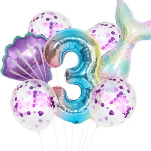 May include: A set of 7 mermaid-themed balloons, including a large iridescent blue number 3 balloon, 4 clear balloons with purple confetti, a purple seashell balloon, and a rainbow iridescent mermaid tail balloon.
