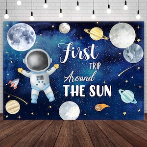 May include: A blue and white space-themed backdrop with an astronaut, planets, stars, and the text "First Trip Around The Sun".