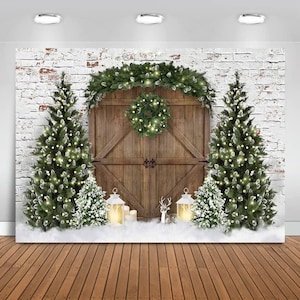 May include: A Christmas-themed backdrop featuring a rustic wooden door, flanked by two decorated Christmas trees with lights. A wreath hangs on the door, and smaller trees and lanterns are in front. The background is a white brick wall.