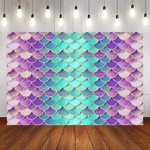 May include: A backdrop featuring a mermaid scale pattern in shades of purple, blue, and turquoise with gold glitter accents. The backdrop is perfect for a mermaid-themed party or photo shoot.
