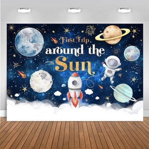 May include: A blue and white space-themed backdrop with a rocket, astronaut, planets, and stars. The text "First Trip around the Sun" is written in gold lettering.