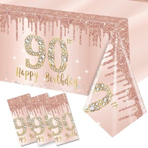 May include: Pink and gold table cover with a glittery finish and the text "90th Happy Birthday".  The table cover is decorated with a dripping effect and a diamond-like design.  There are also four matching napkins with the same design.
