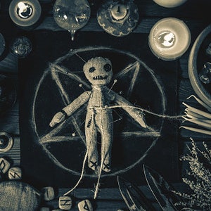 Puede incluir: Una muñeca vudú con alfileres clavados en ella, rodeada de velas, un pentagrama y otros objetos ocultos.