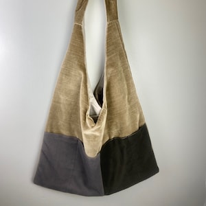 May include: A large, brown, velvet tote bag with two gray fabric pockets on the bottom. The bag has a single, long strap.