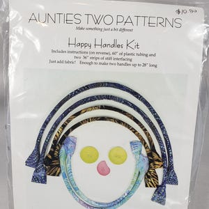 May include: Happy Handles Kit by Aunties Two Patterns. The kit includes instructions, plastic tubing, and interfacing to make two handles up to 71 cm long. The package features colorful fabric samples and buttons.