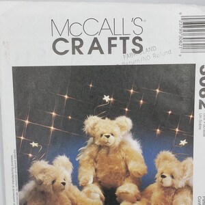 May include: A McCall's Crafts pattern for making straw stocking teddy bears. The image shows three plush teddy bears with light brown fur, set against a blue background with twinkling lights. The pattern includes the text "Straw Stockings".