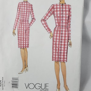 May include: A Vogue Patterns sewing pattern envelope featuring an illustration of a long-sleeved, knee-length dress with a pink and white gingham check pattern, a high neckline with a small ruffle, and a front button closure, size 20.