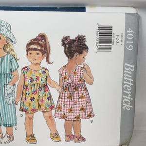 以下が含まれることがあります： 子供服のButterickパターン4019。イラストには、ドレス、ロンパース、帽子など、さまざまな衣装を着た4人の若い女の子が描かれています。衣装は、赤、黄、青の花柄とギンガムチェック柄が特徴です。パターンはサイズ1-2-3用です。