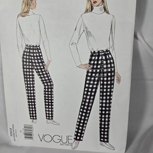 May include: A Vogue Patterns sewing pattern envelope, number 1003, featuring a fashion illustration of a white turtleneck long-sleeve top paired with high-waisted black and white checkered trousers. The design includes a front button closure detail.