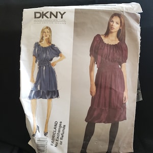 Puede incluir: Un patrón de costura para un vestido con cintura fruncida y un dobladillo con volantes. El patrón es de DKNY, Donna Karan New York, un diseñador estadounidense de Vogue. El patrón incluye dos estilos de vestidos diferentes, uno en azul oscuro y el otro en burdeos.