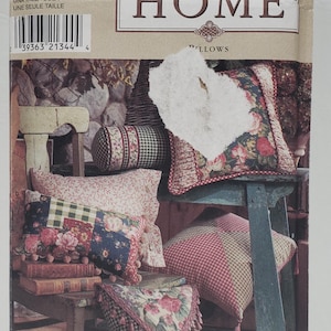 Puede incluir: Un patrón de costura Simplicity Home para almohadas. El número del patrón es 8044. El patrón muestra cinco almohadas diferentes con varios diseños florales y a cuadros. Las almohadas están dispuestas en una silla de madera y un taburete de madera. El patrón se titula "Almohadas" e incluye el texto "Simply...CONCORD".