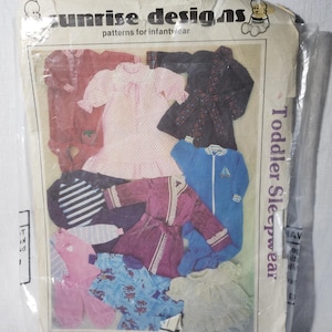 May include: A vintage sewing pattern for toddler sleepwear. The pattern includes designs for a variety of sleepwear items, including a robe, pajamas, and a nightgown. The pattern is from Sunrise Designs, a company that specializes in patterns for infant and toddler clothing.