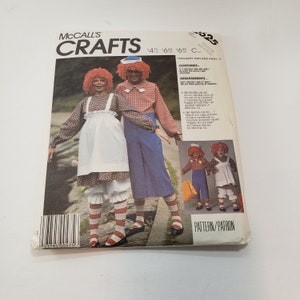 Puede incluir: Un patrón de costura para los trajes de Raggedy Ann y Andy. El patrón es de McCall's Crafts e incluye instrucciones para hacer los trajes para niños y adultos. El patrón está impreso en un fondo blanco con un esquema de color rojo, blanco y azul.