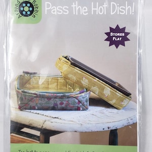 Peut inclure: Emballage plastique transparent contenant deux paniers à plats chauds en tissu. Le texte "Pass the Hot Dish!" est affiché. Les paniers sont conçus pour des plats de 22,86 x 22,86 cm et 22,86 x 33,02 cm. Facile à coudre.