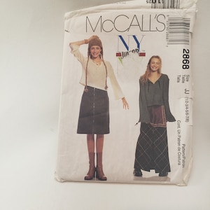 Puede incluir: Un sobre de patrón de costura McCall's vintage. La parte delantera presenta dos modelos con atuendos, incluyendo una falda, un top y un sombrero. El sobre es blanco con texto y números, incluyendo "2868" y "JJ".