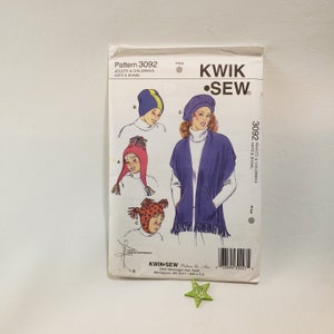 May include: A sewing pattern for hats and a shawl. The pattern is from Kwik Sew and is for adults and children. The pattern shows four different hats, one with a blue and white striped design, one with a red and white striped design, one with a red and white spotted design, and one with a purple and white design. The pattern also shows a purple shawl with a pocket and fringe.