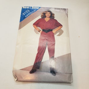 May include: A vintage sewing pattern for a jumpsuit, featuring a woman wearing a red jumpsuit with a black belt. The pattern number is 5123 and the sizes are 8-10-12-14-16. The pattern is from the brand "See & Sew".