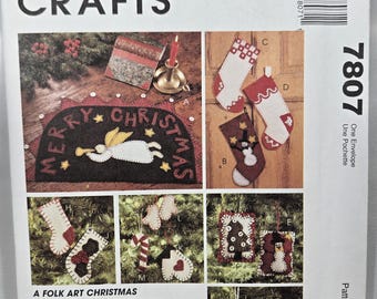 May include: A McCall's Crafts pattern for folk art Christmas ornaments and stockings. The image shows a variety of felt ornaments, stockings, and a penny rug with the words "Merry Christmas".