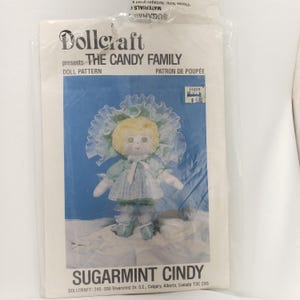 May include: A dollcraft pattern for a doll named Sugarmint Cindy. The pattern is for a doll with a light blue dress, a white bonnet with light blue trim, and blonde hair. The pattern is from Dollcraft, 245-200 Rivercrest Dr. S.E., Calgary, Alberta, Canada T2C 2X5.