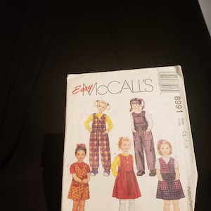 May include: A sewing pattern for children's dungarees. The pattern is for sizes 6, 7, and 8. The pattern shows four different styles of dungarees, including a plaid pair, a solid pair, a floral pair, and a gingham pair.