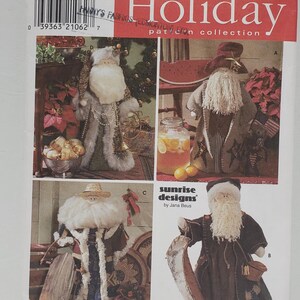 Könnte beinhalten: Eine Simplicity Holiday-Schnittmuster-Kollektion mit vier verschiedenen Weihnachtsmann-Designs. Das Schnittmuster enthält Anleitungen zum Nähen eines Weihnachtsmanns mit roter und weißer Mütze, eines Weihnachtsmanns mit Strohhut, eines Weihnachtsmanns mit blau-weißem Mantel und eines Weihnachtsmanns mit braun-weißem Mantel. Das Schnittmuster trägt den Titel "Sunrise Designs by Jana Beus".