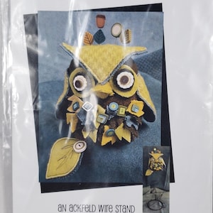 Peut inclure: Un paquet pour un projet de couture de coussin à épingles J. Edgar. Le design présente un hibou en feutre avec des boutons. Le texte indique "Just Another Button Company". Comprend un support en fil métallique Ackfeld.