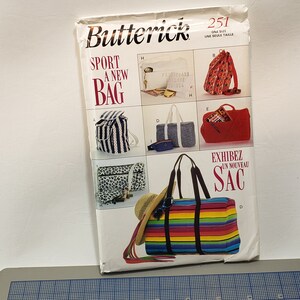 May include: A Butterick sewing pattern envelope featuring various bag designs. The cover displays a striped duffel bag with black handles, a straw hat, and sunglasses. Text includes "SPORT A NEW BAG" and "EXHIBEZ UN NOUVEAU SAC".