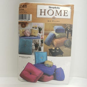 May include: Simplicity Home sewing pattern for box pillows. The pattern shows a variety of pillows in different colors and fabrics, including blue, green, red, and brown. The pattern includes instructions for making the pillows and a list of materials needed.