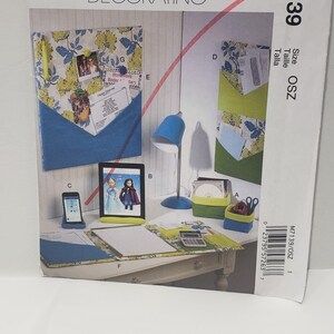 May include: A McCall's Home Decorating pattern packet. The packet features a mock-up of a desk with a blue desk lamp, a tablet, and a framed picture. The packet also shows a wall organizer with pockets.
