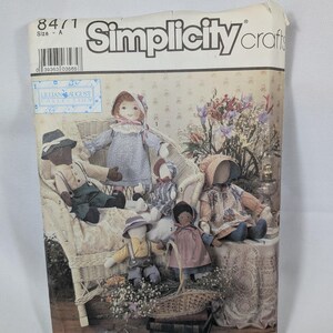 May include: A Simplicity Crafts sewing pattern envelope, number 8471, size A, from the Lillian August Collection. The front features an illustration of five handmade fabric dolls wearing bonnets and hats, seated on a wicker chair with flowers.