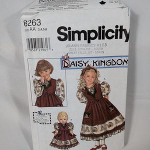 May include: A Simplicity 8263 sewing pattern envelope for a Daisy Kingdom dress and doll outfit. The white paper packaging features illustrations of a child wearing a brown dress with puff sleeves and a matching outfit for a doll, with text.