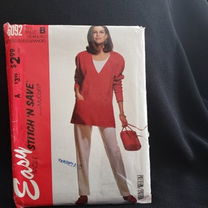 May include: A red sewing pattern for a long-sleeved tunic with a V-neckline and a pocket on the front. The pattern is called "Easy Stitch 'N Save" by McCall's and has the number 6092.
