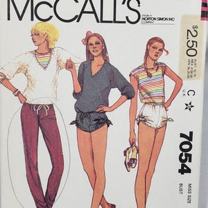 Puede incluir: Sobre de patrón de costura McCall's vintage. La portada presenta ilustraciones de mujeres con atuendos informales, incluyendo un top a rayas y pantalones cortos. El número de patrón es 7054, con un contorno de busto de 82,5 cm.