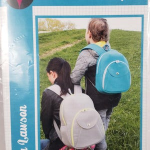 Puede incluir: Un patrón para la mochila Cumberland de Sara Lawson. La imagen muestra dos mochilas, una gris claro y otra turquesa, sobre niños en un campo de hierba. El patrón está etiquetado como "Sew Sweetness".