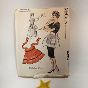 May include: A vintage McCall's sewing pattern for a short apron. The pattern is for misses' or junior sizes and includes instructions for making a short apron with a pocket. The pattern is labeled "Sample" and is printed on a white background with black text.