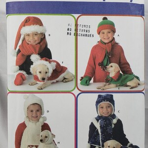 May include: Simplicity sewing pattern featuring children and dogs in festive holiday outfits. The pattern includes options for Santa hats, scarves, and matching dog coats. The pattern number is 3973, with size A for all sizes.