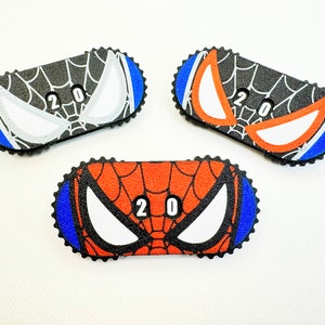 Könnte beinhalten: Drei verschiedene Spider-Man-Gesichtsmasken in Schwarz, Rot und Weiß. Jede Maske hat die Nummer "20" darauf gedruckt.