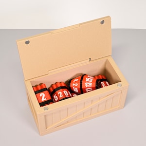 Puede incluir: Una caja de madera con una tapa con bisagras, abierta para revelar un conjunto de palos de dinamita rojos con bandas negras y n&uacute;meros blancos. Los palos est&aacute;n etiquetados con "2", "529", "4 2 20", "11 13 15" y "623".