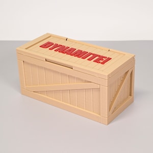 Puede incluir: Una caja de madera de color beige con una etiqueta roja que dice "&iexcl;Dinamita!" en la parte superior.