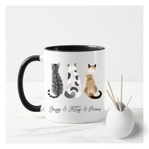 May include: White ceramic mug with a black rim and handle. The mug features a watercolor illustration of three cats sitting back to back. The text "Suzy & Kitty & Meow" is printed below the cats.