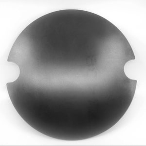 May include: A black metal round pan with two cutouts on the side. The pan is slightly curved and has a matte finish.