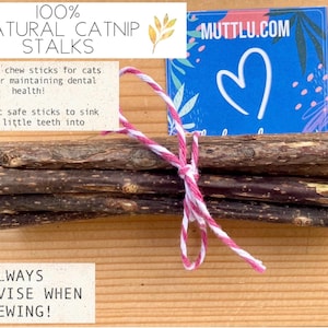May include: A bundle of brown catnip sticks tied with pink and white twine. The sticks are labeled "100% Natural Catnip Stalks" and "Always Supervise When Chewing!"  The label also includes the website "muttlu.com".