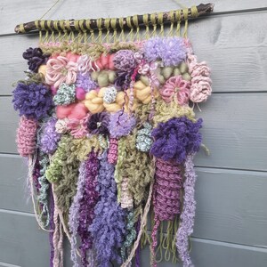 May include: A colorful wall hanging made of yarn and fabric in shades of pink, purple, green, and yellow. The hanging features a variety of textures and patterns, creating a unique and eye-catching piece of art.