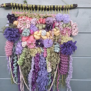May include: A colorful wall hanging made of yarn and fabric. The hanging features a variety of textures and colors, including pink, purple, green, and yellow. It is a unique and eye-catching piece of art.