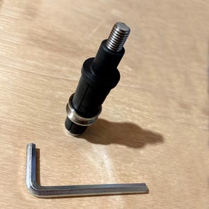 以下が含まれることがあります： ねじ山のある金属端と銀色のリングが付いた黒いコンポーネントと、銀色のL字型六角レンチ。 このコンポーネントは、より大きなメカニズムまたはデバイスの一部であるようです。