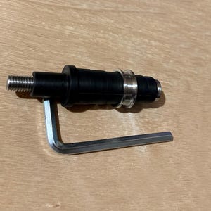 以下が含まれることがあります： 黒い円筒形の部品で、ねじ付きの金属端と透明なリングがあり、銀色のL字型六角レンチが付属しています。これは、より大きなメカニズムの一部であるようです。
