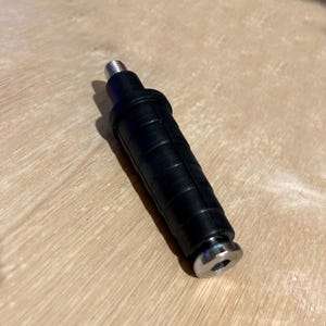 以下が含まれることがあります： 黒いゴムと金属の物体で、ねじ山のある上部と金属製のベースが付いています。 オブジェクトは円筒形で、ゴム部分にはリブ状のテクスチャがあります。 金属ベースの中央には穴があります。