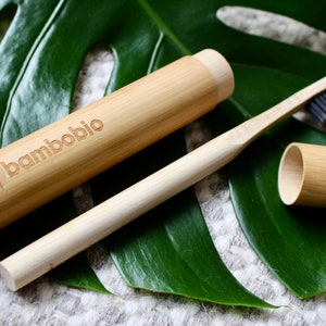 Könnte beinhalten: Eine Bambuszahnbürste und ein Bambus-Etui mit dem Text "bambobio" darauf. Die Zahnbürste und das Etui liegen auf einem grünen Blatt.