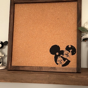 May include: A brown wooden framed corkboard with a black silhouette of Mickey Mouse's head with Chip and Dale inside.