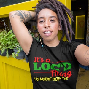 Può includere: Una maglietta nera con il testo "It's a Loc'd Thing You Wouldn't Understand" in lettere verdi, rosse e gialle. Il modello indossa la maglietta e ha i dreadlocks.